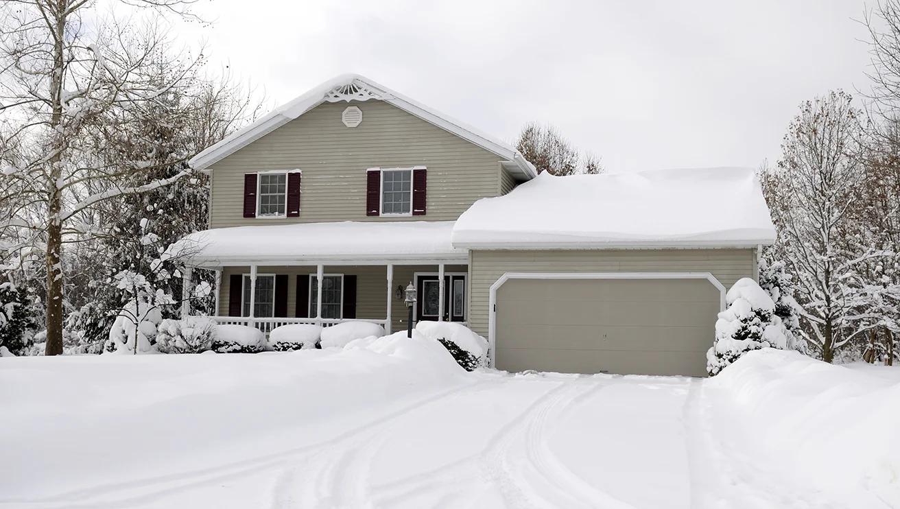 Snow blanketing a single-family home and its front yard.